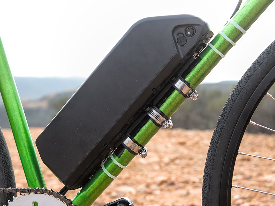 A black e-bike battery mounted on a green down tube, with its power switch and charge port